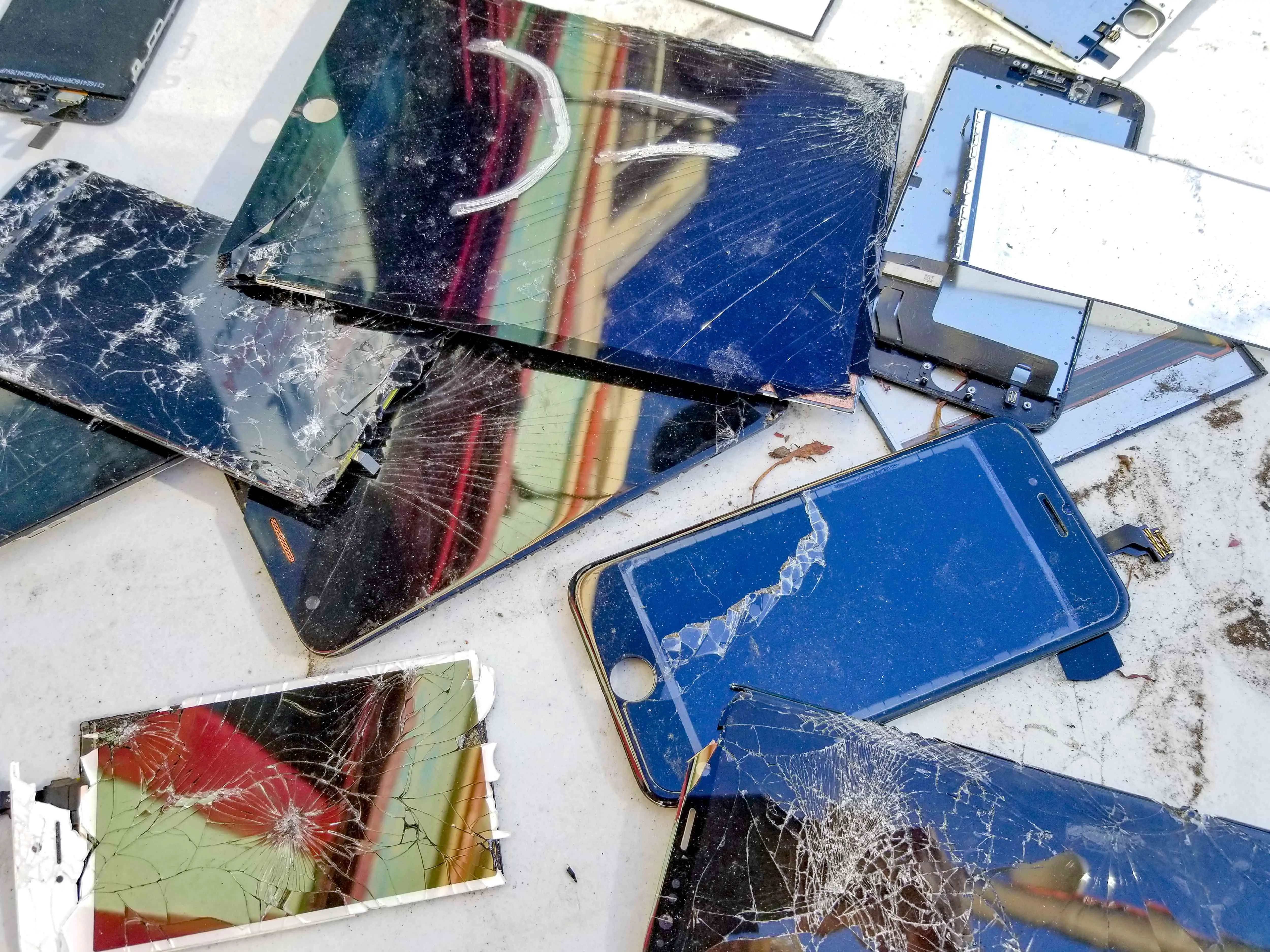 Vários smartphones e tablets quebrados com telas rachadas em uma mesa.