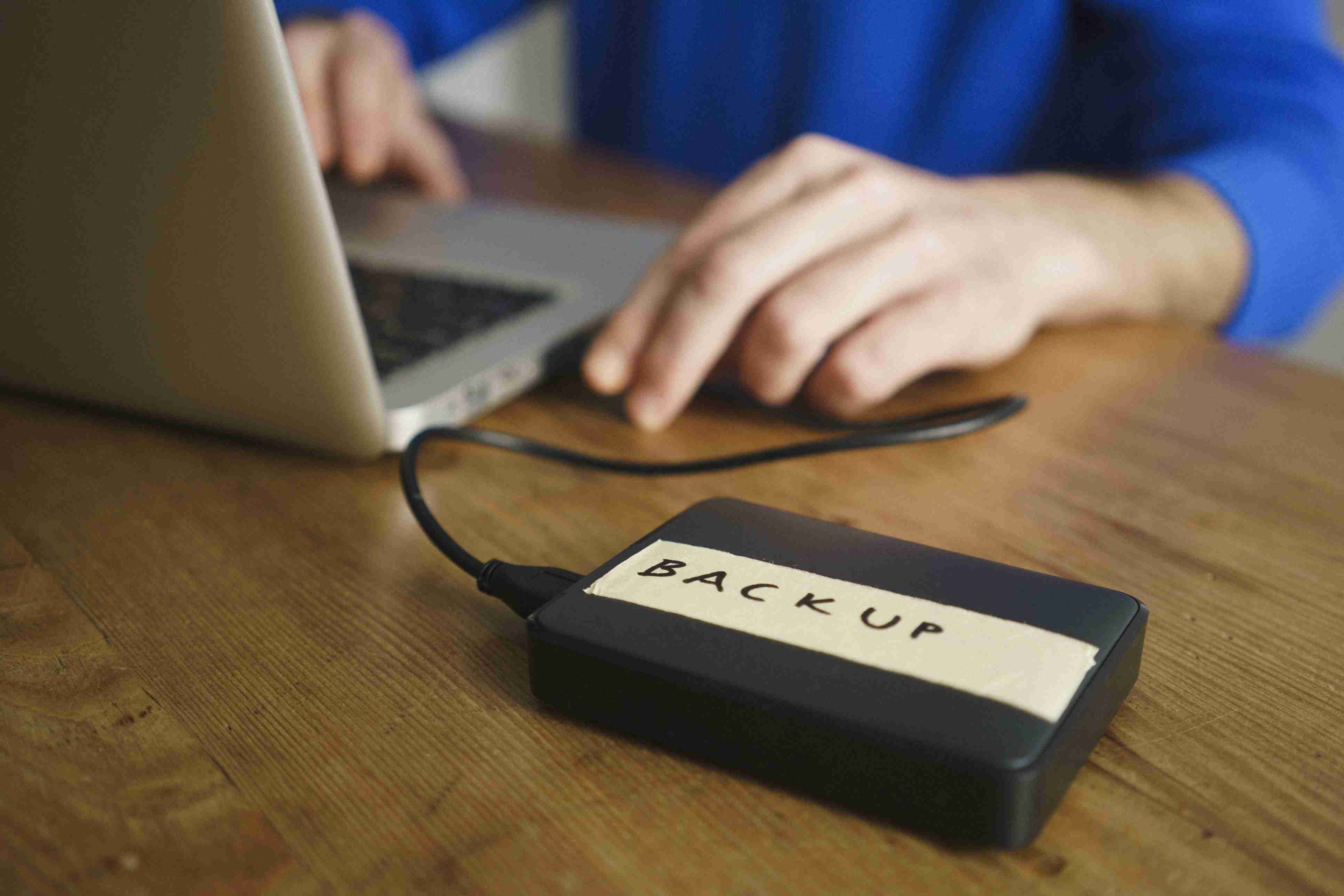 Pessoa usando laptop com etiqueta de backup no disco rígido externo na mesa