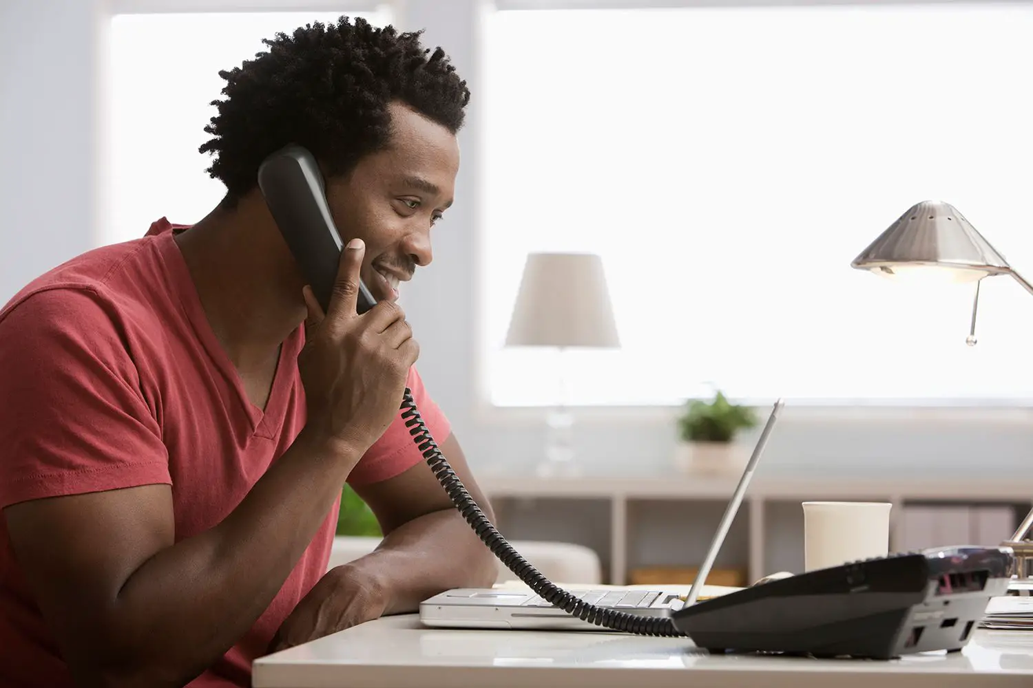 Homem negro sorridente falando ao telefone no escritório em casa