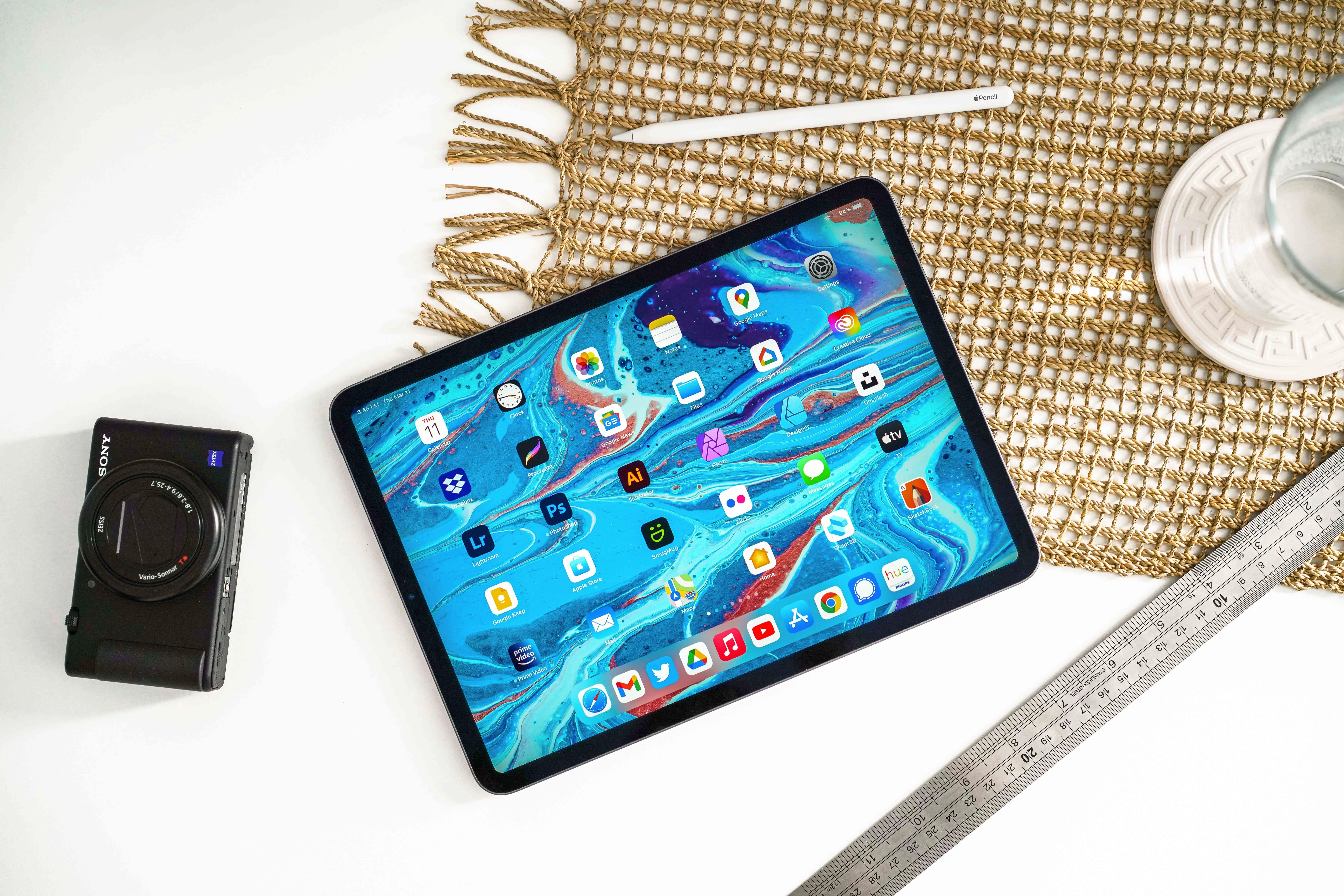 Um iPad Pro com um lápis de maçã sobre uma superfície branca com uma câmera, régua e vidro por perto.