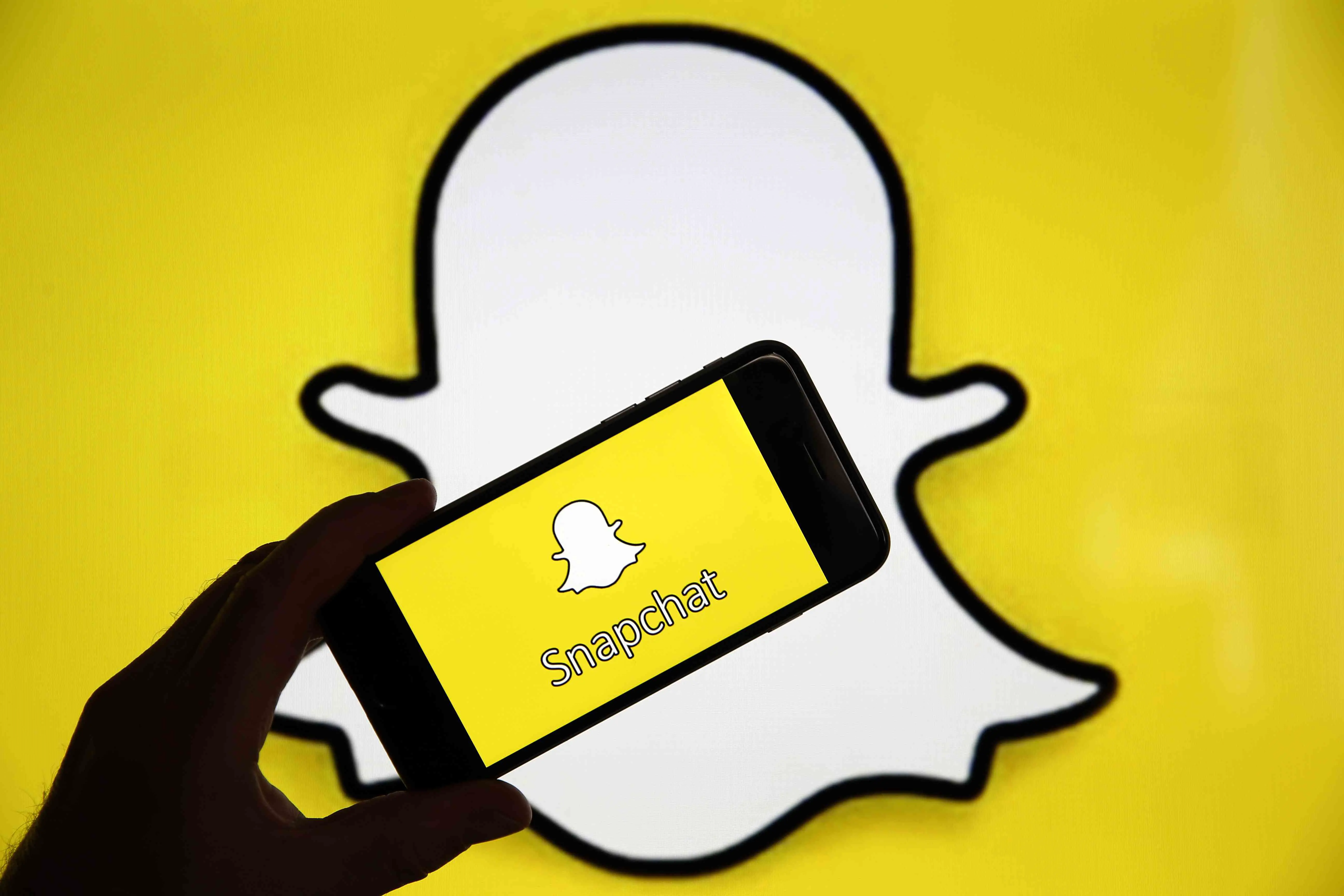 Logotipo do Snapchat atrás da mão segurando o Snapchat em um telefone