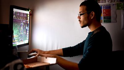 Homem de óculos jogando videogame em seu PC em um quarto escuro