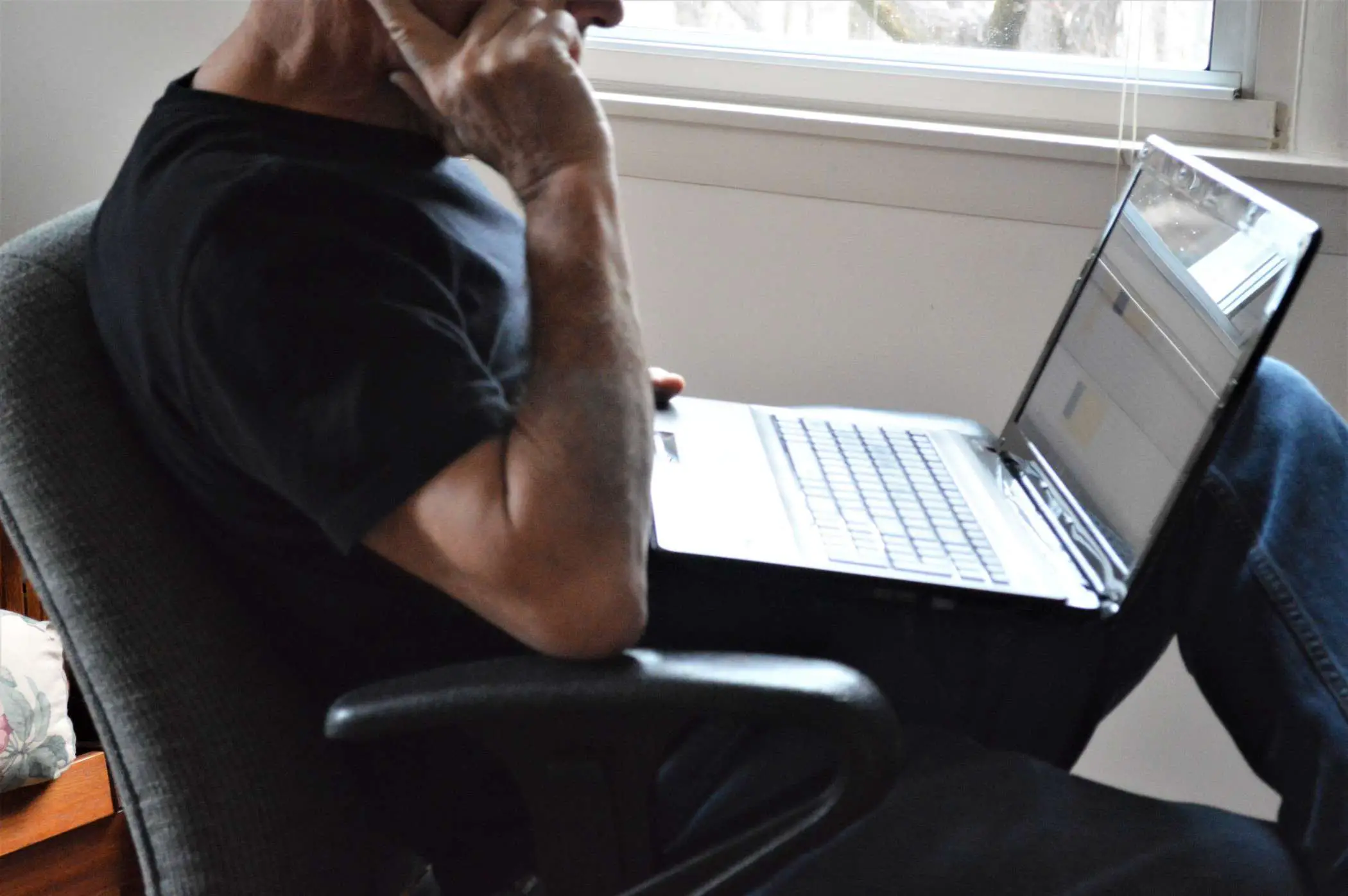 Um homem usando um laptop Windows perto de uma janela.