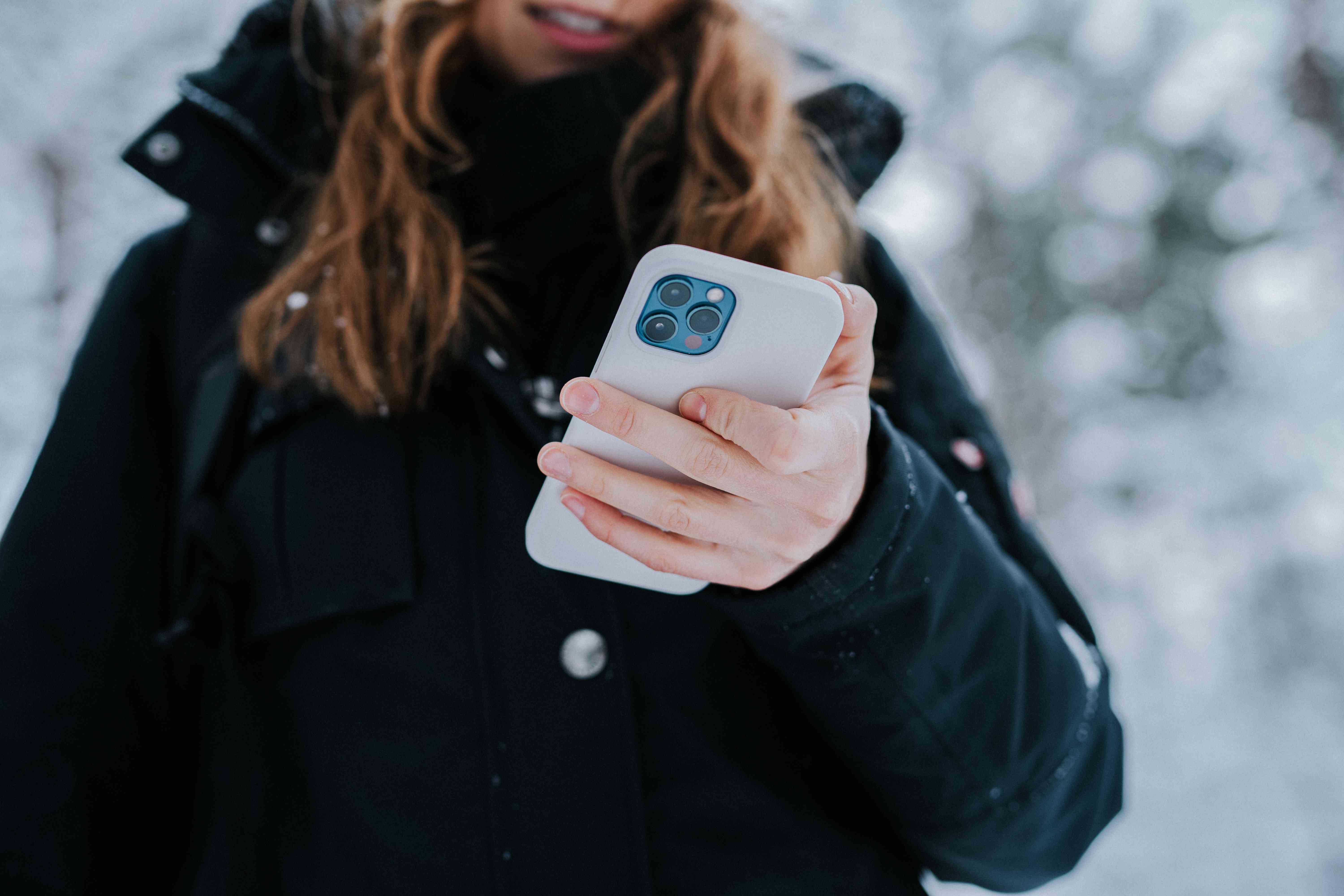 Uma pessoa ao ar livre, durante o inverno, segurando um iPhone 12.