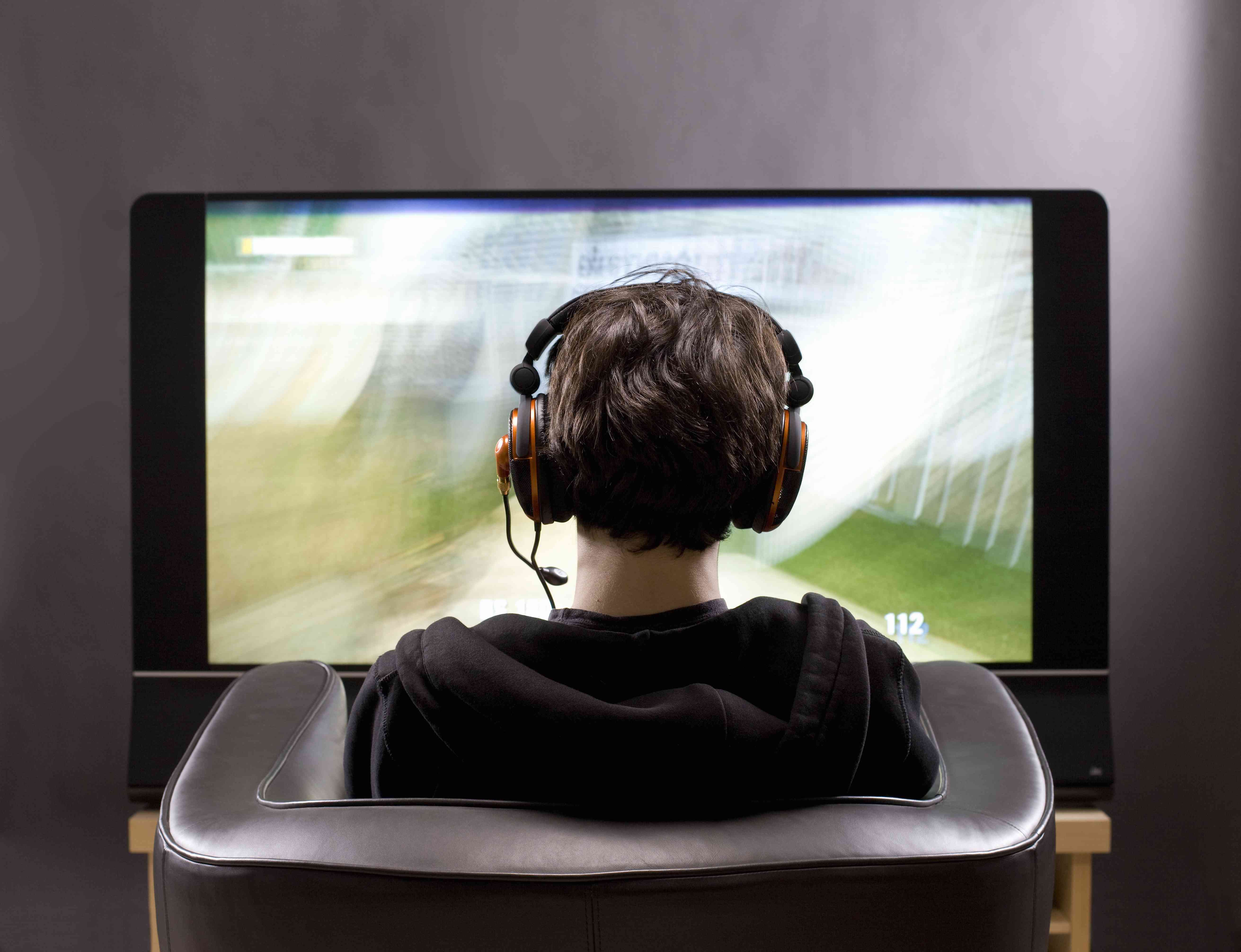 Adolescente sentado em frente à TV jogando videogame